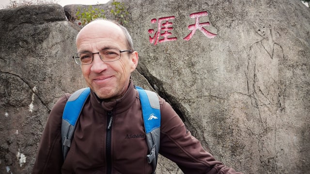 Ein Mann steht vor einem Stein mit chinesischen Schriftzeichen und einem Porträt einer Frau Ein Mann steht vor einem Stein mit chinesischen Schriftzeichen und einem Porträt einer Frau