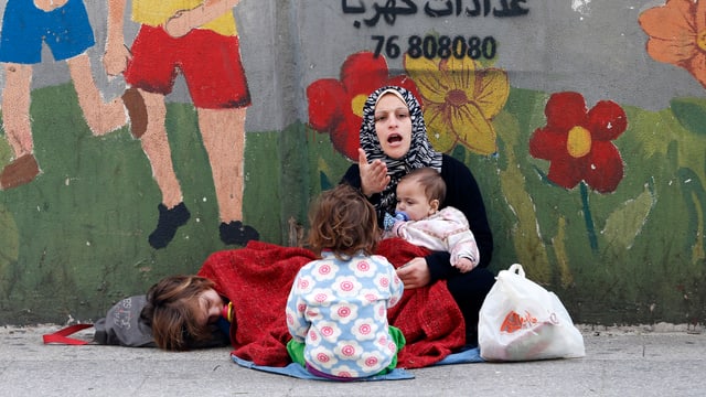 Eine Frau sitzt mit ihren Kindern am Strassenrand