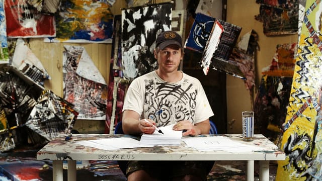 Mann um die 30ig sitzt in einem bunten Atelier Mann um die 30ig sitzt in einem bunten Atelier