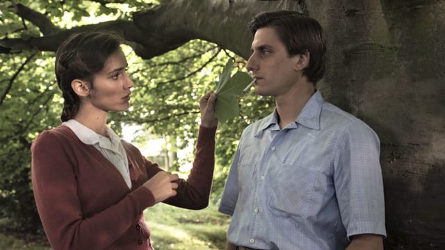 Mann und Frau stehen unter einem Baum, sie hält ihm ein Baumblatt ins Gesicht. Mann und Frau stehen unter einem Baum, sie hält ihm ein Baumblatt ins Gesicht.