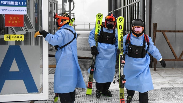 Chinesen steigen in Schutzanzüge eingehüllt vom Skilift.