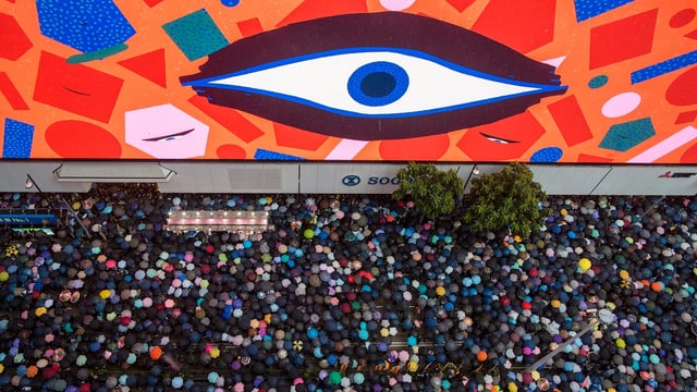 Ein grosses Auge an einer Wand. Vor der Wand sind viele Protestierende. Ein grosses Auge an einer Wand. Vor der Wand sind viele Protestierende.