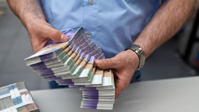 Ein Mann hält ein Bündel 1000er-Noten. Ein Mann hält ein Bündel 1000er-Noten.