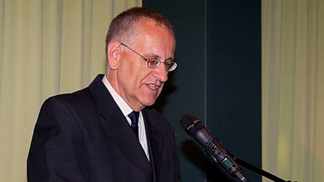 Schuler in schwarzem Anzug spricht in ein Mikrofon. Schuler in schwarzem Anzug spricht in ein Mikrofon.