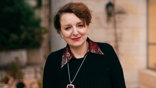 Eine Frau mit schwarzem Pullover vor einer Hausfassade. Sie schaut in die Kamera. Eine Frau mit schwarzem Pullover vor einer Hausfassade. Sie schaut in die Kamera.