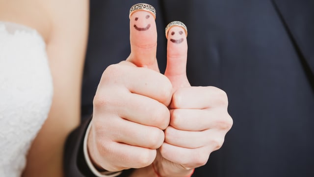 Brautpaar das Daumen mit aufgemalten Gesichtern hochhält. Brautpaar das Daumen mit aufgemalten Gesichtern hochhält.