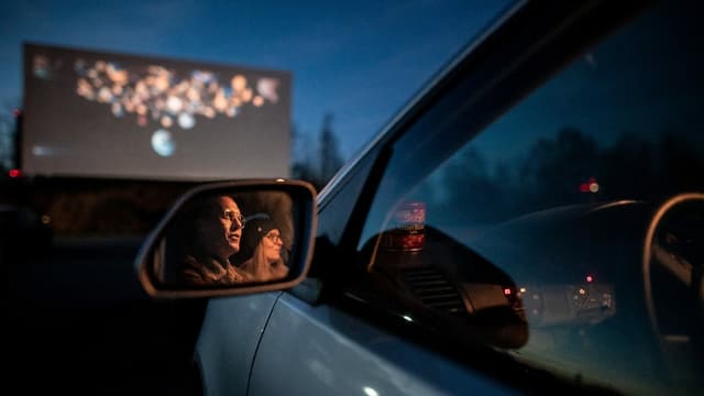 Ein paar sitzt in einem Auto und schaut auf die Leinwand des Auto-Kinos. Ein paar sitzt in einem Auto und schaut auf die Leinwand des Auto-Kinos.