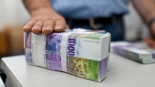 Ein Mann hält seine Hand auf ein Bündel 1000er Noten. Ein Mann hält seine Hand auf ein Bündel 1000er Noten.