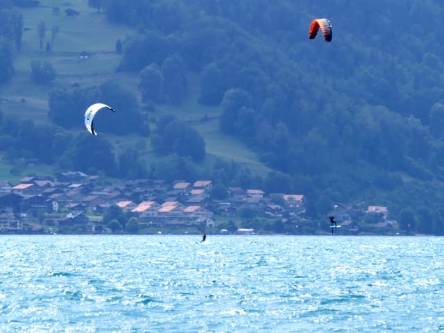 Zwei Kitesurfe lassen sich vom Wind über den See ziehen. Zwei Kitesurfe lassen sich vom Wind über den See ziehen.