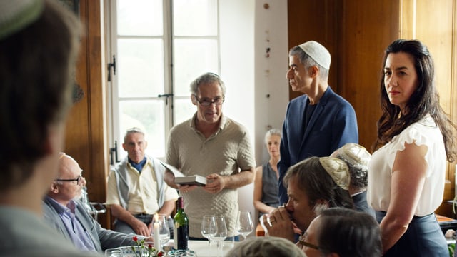 Eine Gruppe von Leuten sitzt und steht um eine grosse Tafel. Eine Gruppe von Leuten sitzt und steht um eine grosse Tafel.