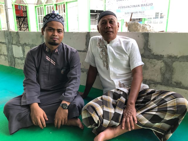 Imam und weiterer Mann sitzen im Schneidersitz auf dem Boden der zerstörten Moschee. Imam und weiterer Mann sitzen im Schneidersitz auf dem Boden der zerstörten Moschee.