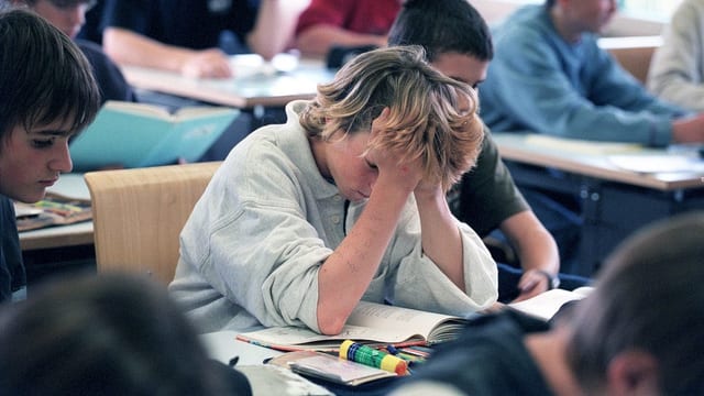 Ein Bub im Klassenzimmer. Er stützt seinen Kopf in seinen Händen. Ein Bub im Klassenzimmer. Er stützt seinen Kopf in seinen Händen.