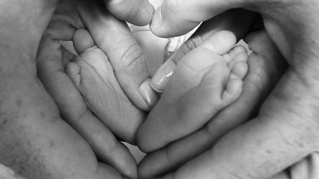 Kleine Baby-Füsse in der Mitte, vier Hände formen ein Herz drum herum. Kleine Baby-Füsse in der Mitte, vier Hände formen ein Herz drum herum.