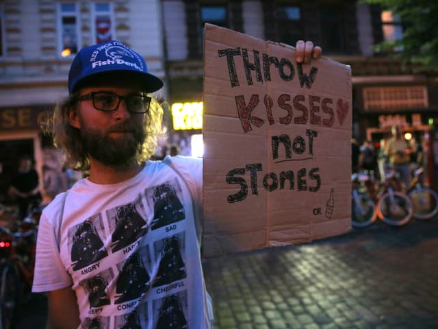 Demonstrant hält Schild mit der Aufschrift «Throw kisses, not stones».