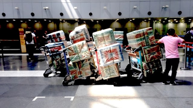 Mensch mit Gepäckwagen mit bunt eingepackter Schmuggelware Mensch mit Gepäckwagen mit bunt eingepackter Schmuggelware