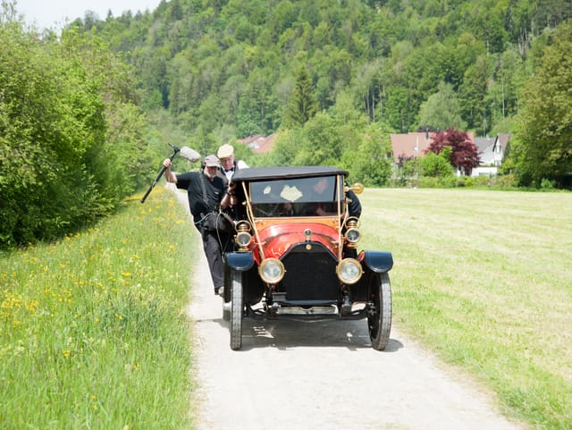 Tontechniker klammert sich am Oldtimer fest, Fahrt auf Kiesweg im Grünen