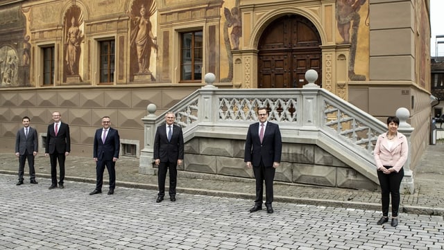 Fünf Männer und eine Frau stehen mit grossem Abstand vor dem Schwyzer Regierungsgebäude.