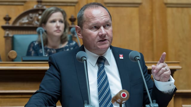 Mann, der am Rednerpult steht mit erhobenem Zeigfinger Mann, der am Rednerpult steht mit erhobenem Zeigfinger