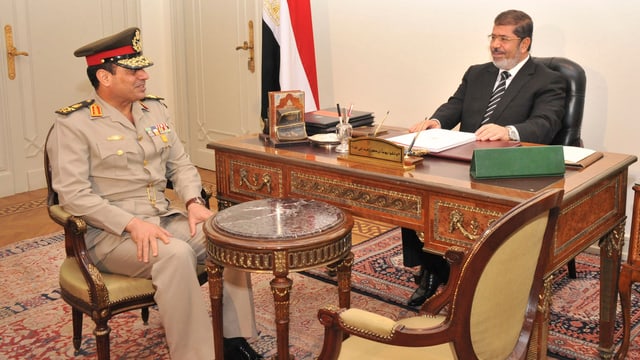 Abdul Fatah Kahlil Sisi (links) und Mohammed Mursi (rechts) sitzen sich an einem Tisch gegenüber.
