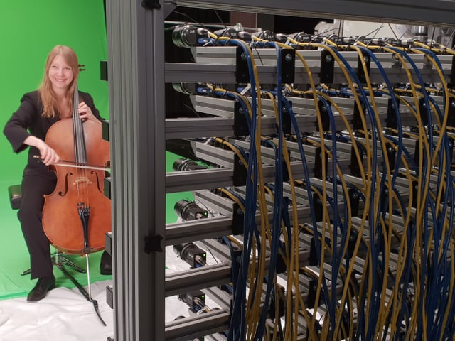 Die Cellistin Cellistin Isabell sitzt vor einem grünen Tuch auf einem Stuhl, vor ihr das Lichtfeld-Rig mit 64 kleinen Kameralinsen. Die Cellistin Cellistin Isabell sitzt vor einem grünen Tuch auf einem Stuhl, vor ihr das Lichtfeld-Rig mit 64 kleinen Kameralinsen.