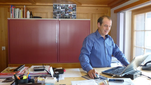 Beat Zenklusen en ina chamischa blaua davos in pult aut che lavura cun in laptop. Sin maisa ins vesa massa palpiri, dossiers, plans ed in func. Beat Zenklusen en ina chamischa blaua davos in pult aut che lavura cun in laptop. Sin maisa ins vesa massa palpiri, dossiers, plans ed in func.
