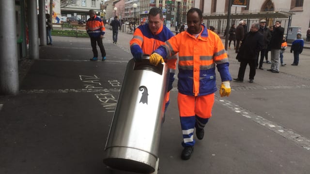 Männer transportieren einen Mülleimer. Männer transportieren einen Mülleimer.