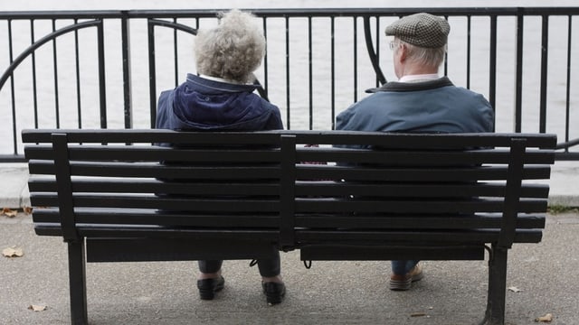 Ein Rentner-Ehepaar sitzt auf einer Bank vor einem See