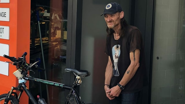 Ein Mann mit Kappe steht vor einer Migros. Ein Mann mit Kappe steht vor einer Migros.
