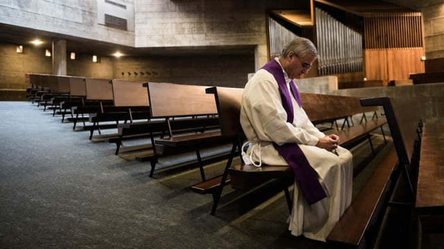 Leere Kirche. Nur ein Pfarrer sitzt in einer Reihe und blickt zu Boden. Leere Kirche. Nur ein Pfarrer sitzt in einer Reihe und blickt zu Boden.
