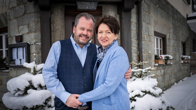 eine Frau und ein Mann stehen vor einem Hoteleingang im Schnee eine Frau und ein Mann stehen vor einem Hoteleingang im Schnee