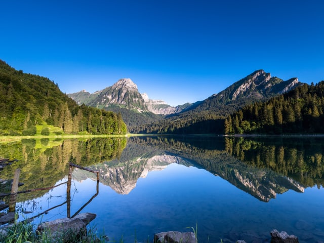 Der blaue Himmel und die Berglandschaft spiegelt sich im glatten See.