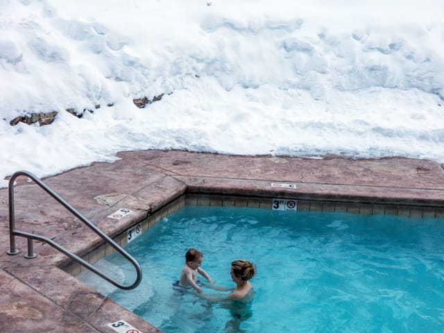 Frau mit kleinem Kind in Pool, daneben liegt Schnee Frau mit kleinem Kind in Pool, daneben liegt Schnee