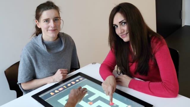 Zwei Frauen sitzen am Tisch und schauen in die Kamera. Zwei Frauen sitzen am Tisch und schauen in die Kamera.