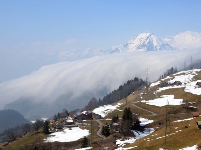 Vordergrund Berghang mit Schneeflecken. Dahinter Wolken-"Wasserfall".