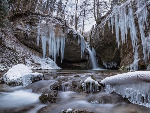 Bach mit Eis und Eiszapfen am Ufer an den Steinen.