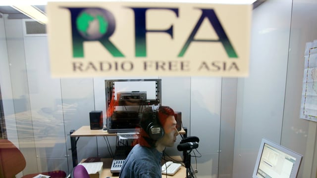 Eine Logo von Radio Free Asia unscharf im Vordergrund, hinten ein Mann am Mikrofon. Eine Logo von Radio Free Asia unscharf im Vordergrund, hinten ein Mann am Mikrofon.