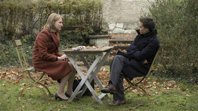 Filmstill: Eine Frau und ein Mann sitzen an einem Gartentisch. Filmstill: Eine Frau und ein Mann sitzen an einem Gartentisch.