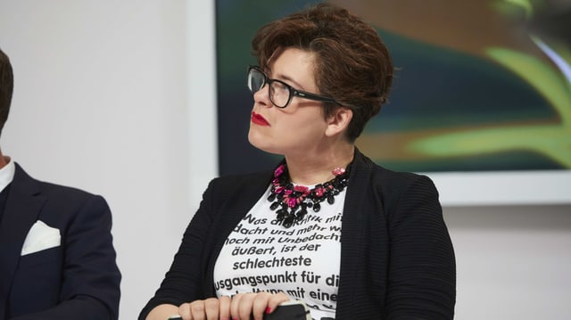 Eine Frau mit kurzen Haaren trägt ein weisses, mit viel Text bedrucktes Shirt. Eine Frau mit kurzen Haaren trägt ein weisses, mit viel Text bedrucktes Shirt.