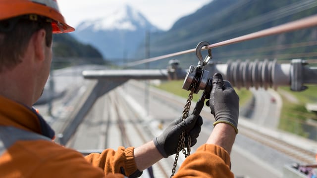 Ein Arbeiter in oranger Kleidung montiert ein Kabel. Ein Arbeiter in oranger Kleidung montiert ein Kabel.