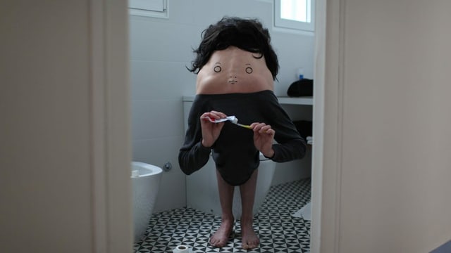 Ein Mensch mit vorübergebeugtem nackten Rücken, auf den ein Gesicht gemalt ist. Ein Mensch mit vorübergebeugtem nackten Rücken, auf den ein Gesicht gemalt ist.