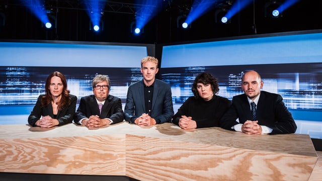 Michael Elsener sitzt mit dem Ensemble an einem massiven Holztisch im Studio. Alle fünf haben die Hände vor sich auf dem Tisch verschränkt. Michael Elsener sitzt mit dem Ensemble an einem massiven Holztisch im Studio. Alle fünf haben die Hände vor sich auf dem Tisch verschränkt.