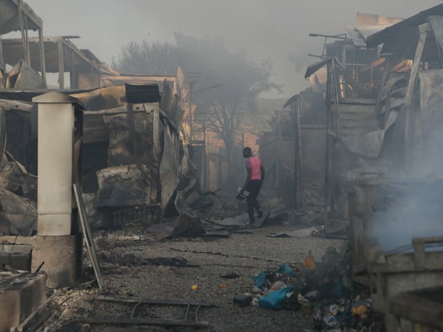 Ein Mann sucht zwischen den Tr&uuml;mmern im Rauch nach &Uuml;berresten.