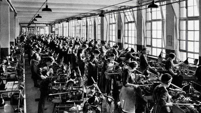 Ein Schwarz-Weiss-Bild: Viele Frauen und Männer arbeiten in einer Revolver-Dreherei. Ein Schwarz-Weiss-Bild: Viele Frauen und Männer arbeiten in einer Revolver-Dreherei.