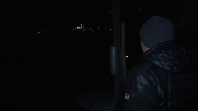 Ein Mann mit dunkler Daunenjacke läuft zum Dorf Surrein, wo nur einzelne Fenster beleuchtet sind. Ein Mann mit dunkler Daunenjacke läuft zum Dorf Surrein, wo nur einzelne Fenster beleuchtet sind.