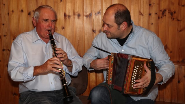 Der Vater spielt Klarinette, der Sohn Schwyzerörgeli. Die Formation musiziert sitzend vor einer getäferten Wand. Der Vater spielt Klarinette, der Sohn Schwyzerörgeli. Die Formation musiziert sitzend vor einer getäferten Wand.