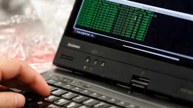 Eine Hand bedient ein Notebook, darauf sind grüne Programmiercodes auf schwarzem Hintergrund zu sehen Eine Hand bedient ein Notebook, darauf sind grüne Programmiercodes auf schwarzem Hintergrund zu sehen