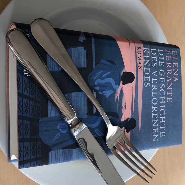 Das Buch «Die Geschichte des verlorenen Kindes» von Elena Ferrante liegt auf einem weissen Teller. Messer und Gabel nebeneinander darüber. Das Buch «Die Geschichte des verlorenen Kindes» von Elena Ferrante liegt auf einem weissen Teller. Messer und Gabel nebeneinander darüber.