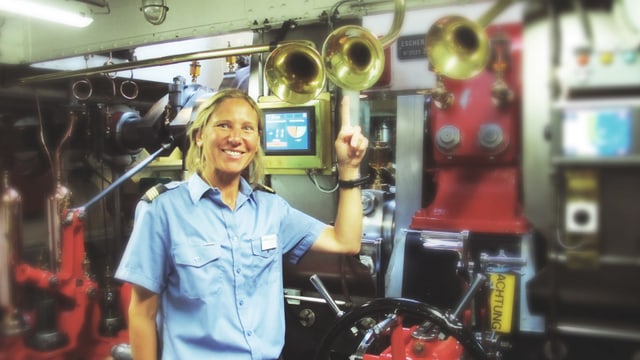 Eine Frau in blauem Hemd steht im Maschinenraum eines Schiffes. Eine Frau in blauem Hemd steht im Maschinenraum eines Schiffes.