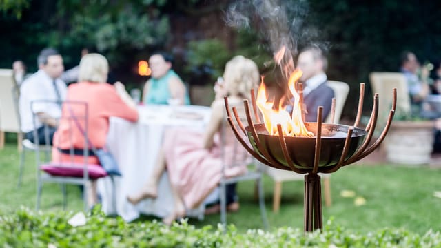 Mehrere Tische in einem Garten mit Leuten, die etwas trinken. Mehrere Tische in einem Garten mit Leuten, die etwas trinken.