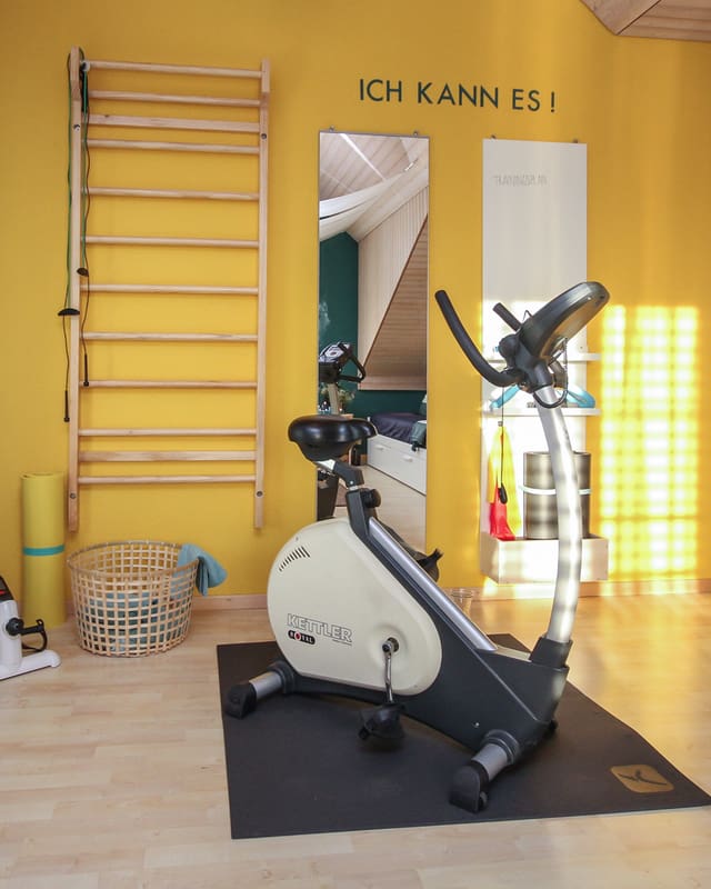 Im umgebauten Fitnessbereich konzentriert sich fast alles auf eine gelb gestrichene Wand. Daran sind eine Sprossenwand, ein Spiegel und ein Workoutboard aufgehängt. Davor steht ein Hometrainer. Im umgebauten Fitnessbereich konzentriert sich fast alles auf eine gelb gestrichene Wand. Daran sind eine Sprossenwand, ein Spiegel und ein Workoutboard aufgehängt. Davor steht ein Hometrainer.